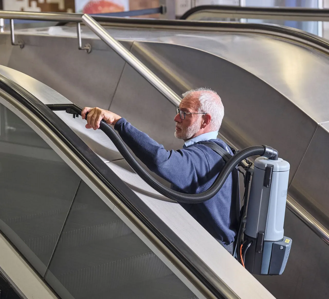 Asito-medewerker reinigt de leuning van een roltrap met een speciale stofzuiger voor een veilige en hygiënische uitstraling