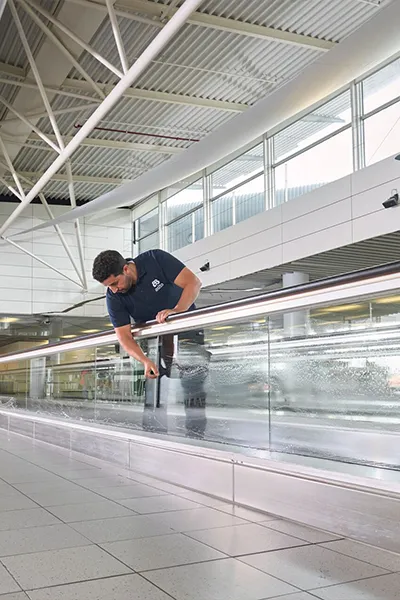 Asito-medewerker maakt de glazen wanden van een rolpad schoon op een luchthaven, voor een representatieve en frisse omgeving voor reizigers.