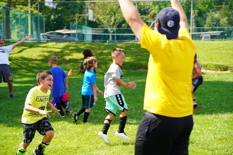 A camp counsellor and campers playing soccer outdors
