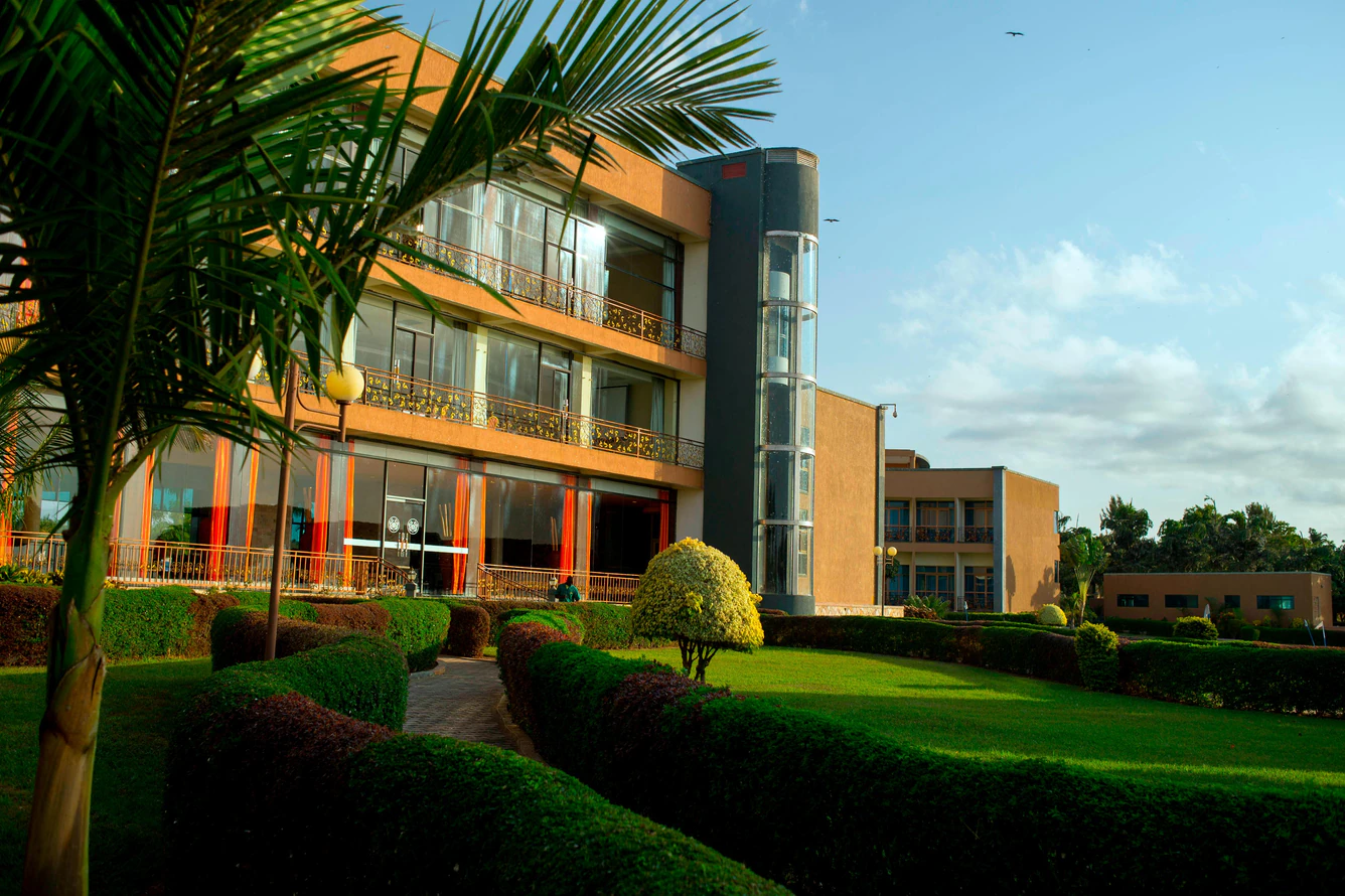 The exterior of the hotel is shown in afternoon light. A palm tree and green lawn is shown in the foreground with the three story building in the background.