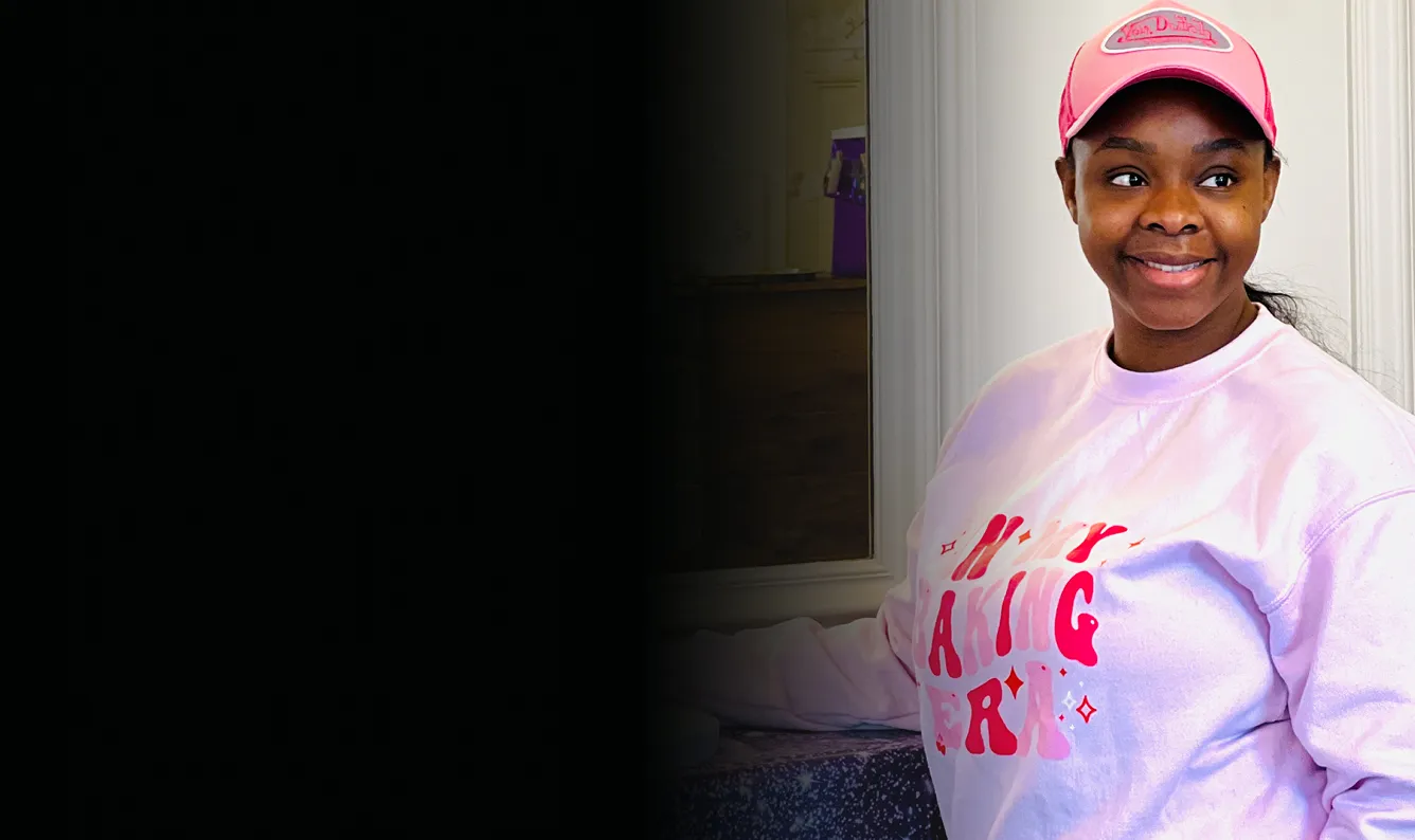 Smiling young woman in a pink cap and pale pink sweatshirt looking off to the side.