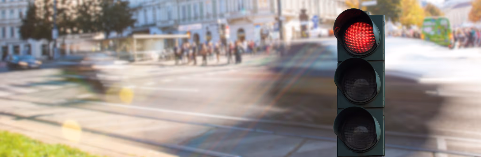 Eine Innenstadt, verschwommen im Hintergrund. Rote Ampel rechts und hervorgehoben im Vordergrund.