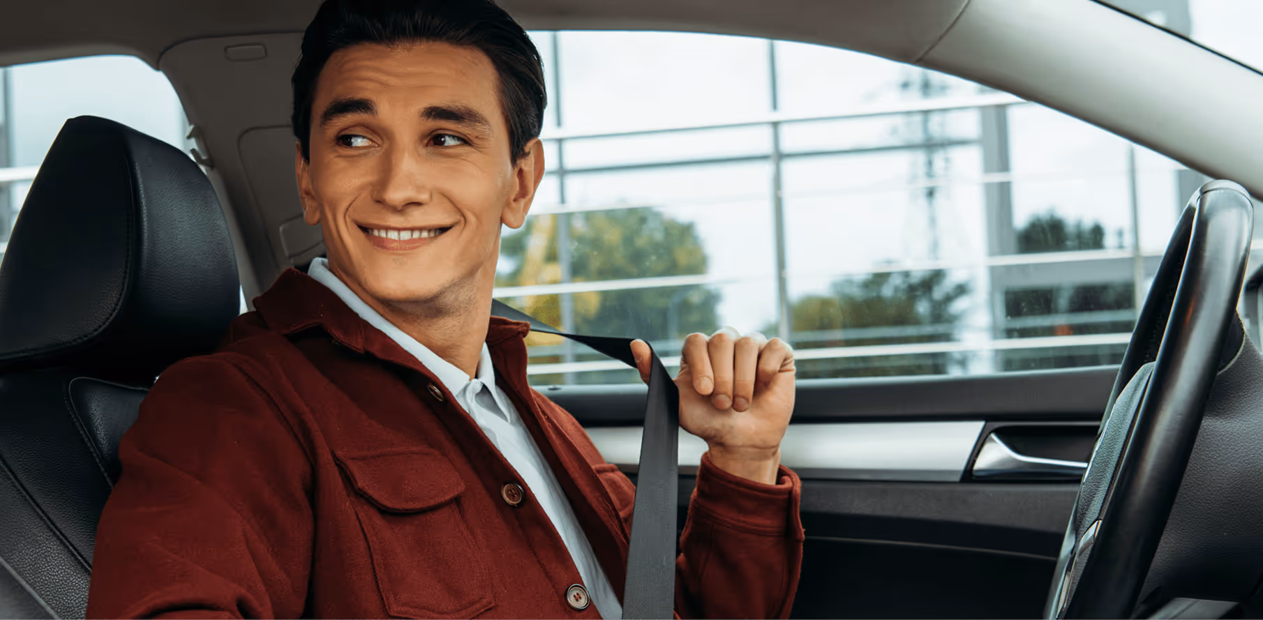 Ein Mann sitzt in seinem Auto und schaut freundlich nach links, während er sich anschnallt.