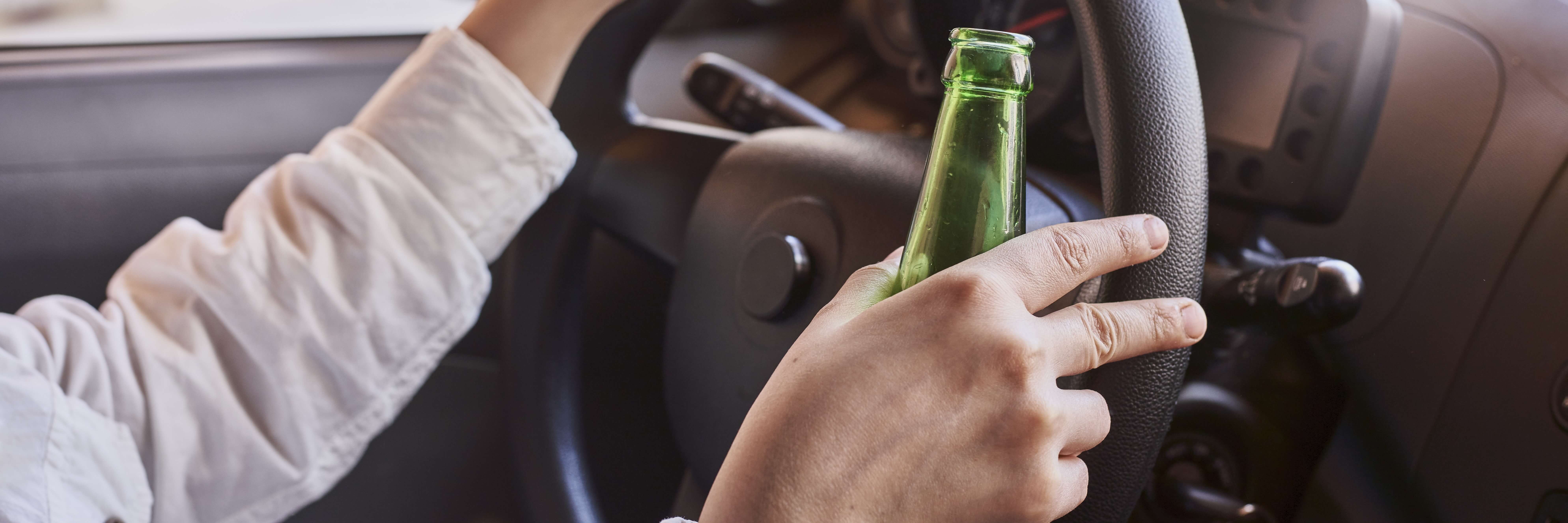 Ein Mann hält eine Bierflasche am Steuer seines Autos.