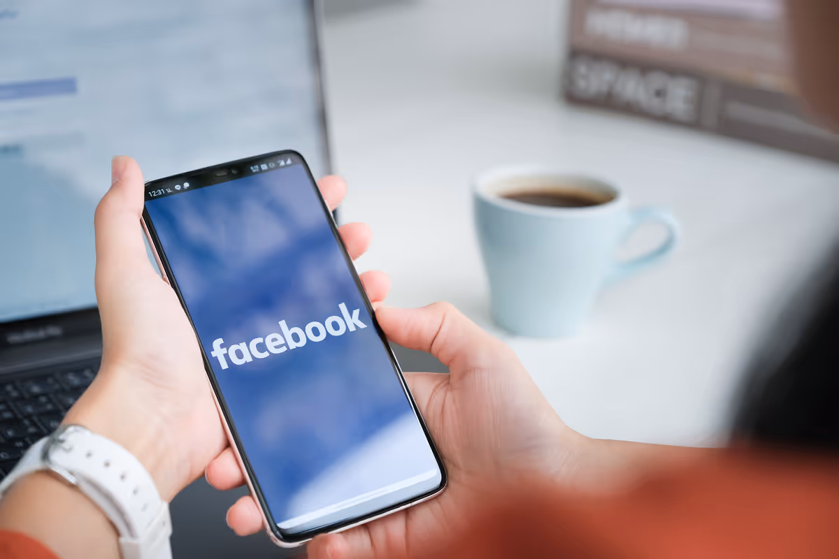 Eine Person öffnet die Facebook App auf dem Handy