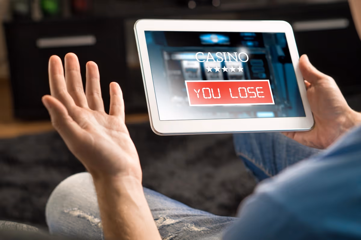 Ein Mann hält ein IPad das zeigt, dass er im Online Casino verloren hat.