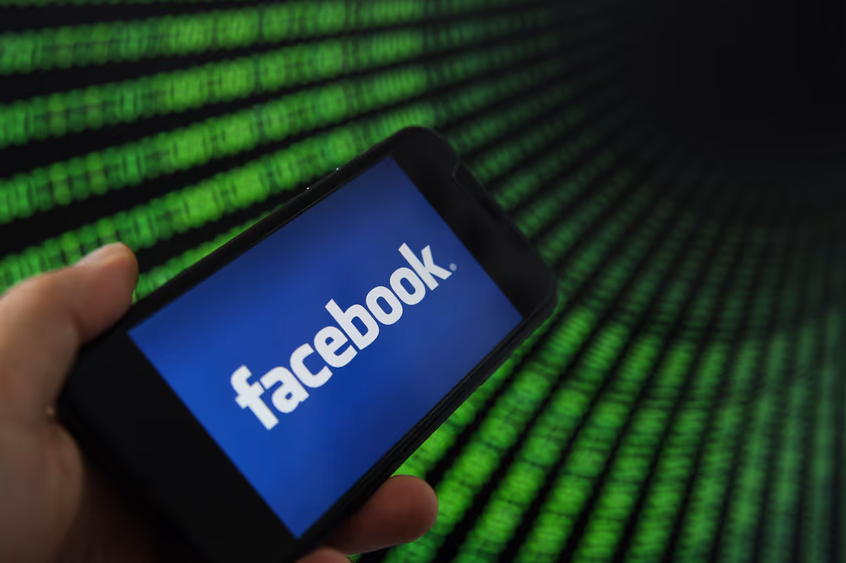 Ein Handy mit Facebook App vor einem Hintergrund mit grünem Code