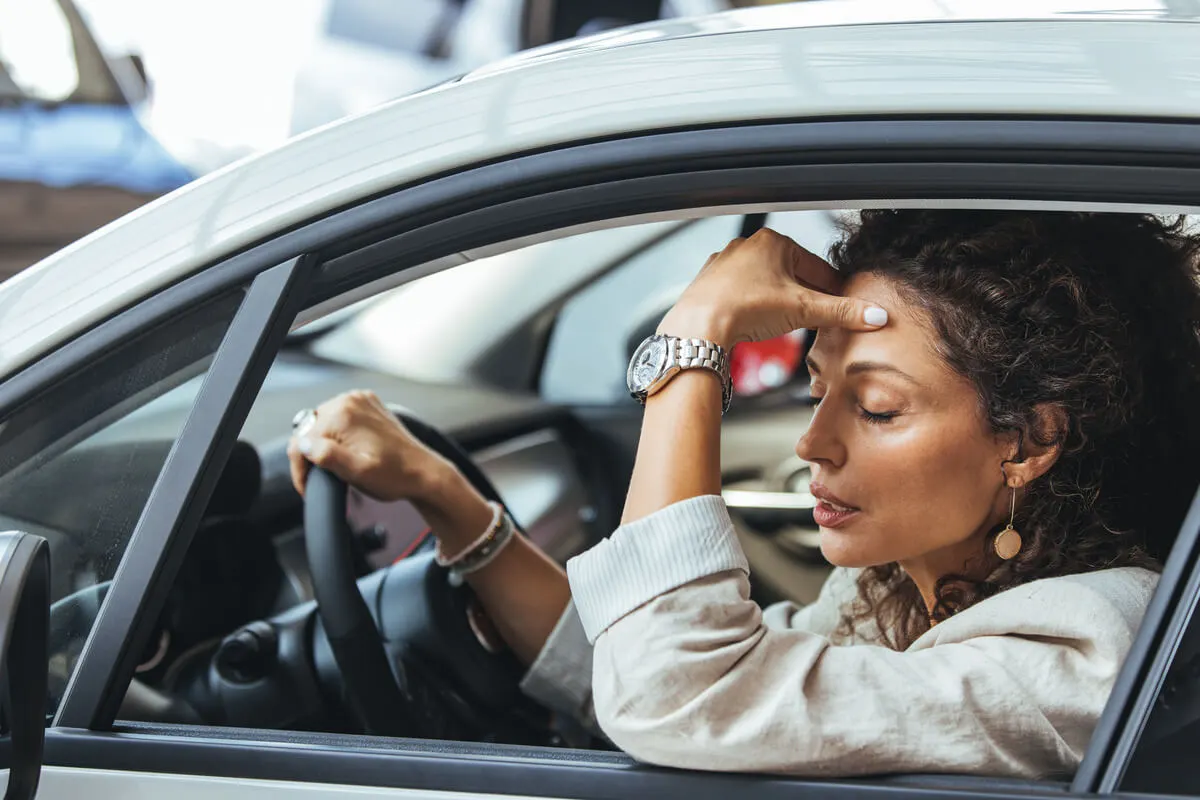 Eine Frau sitzt in ihrem Auto und ärgert sich.
