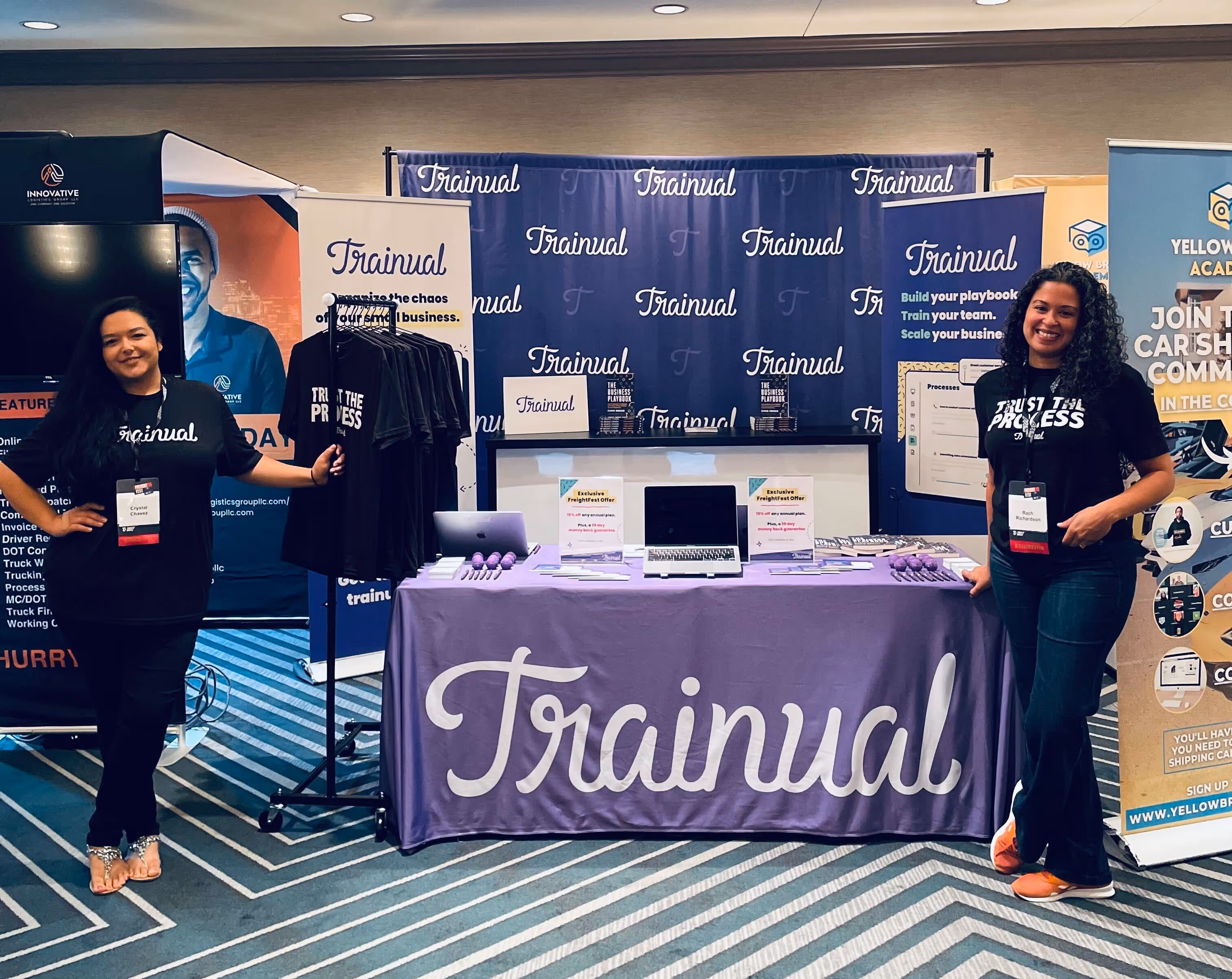 Two women posing in front of a "Trainual" conference booth.