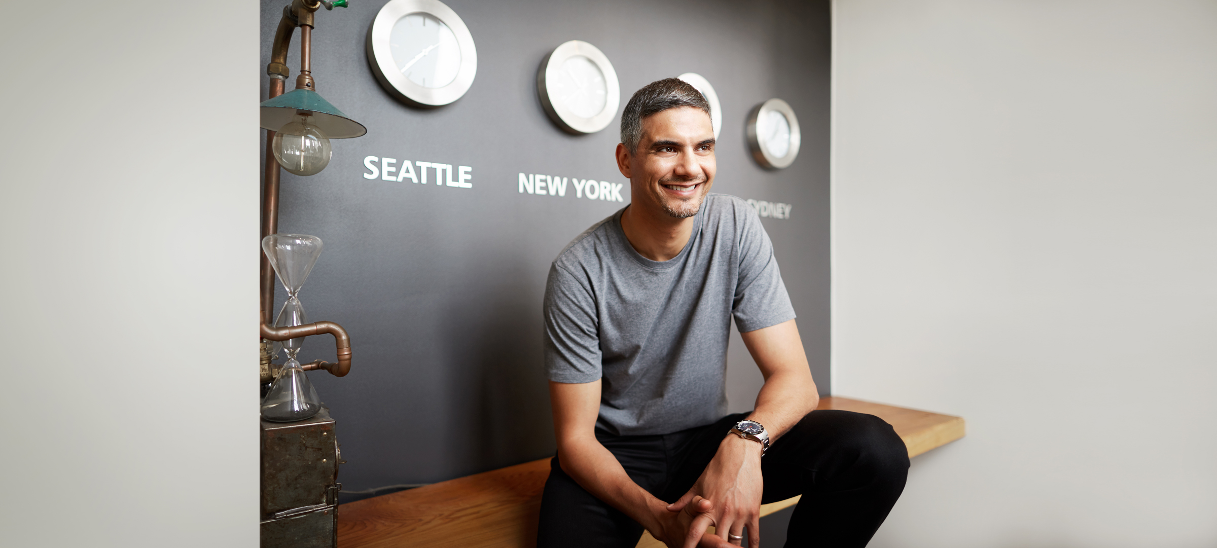 Photo: Male, sitting on a desk, smiling.