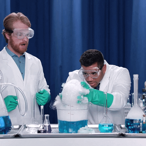 A man in a lab coat lifts and breaks suds from plastic container.