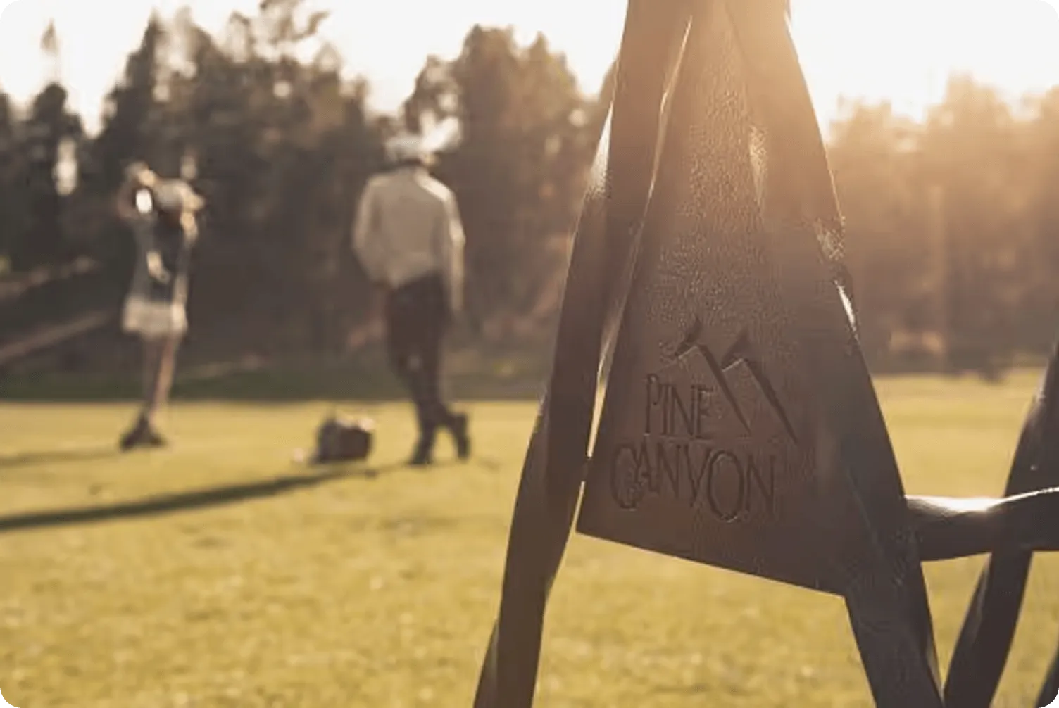 Golfers on a sunlit course with a Pine Canyon sign in the foreground.