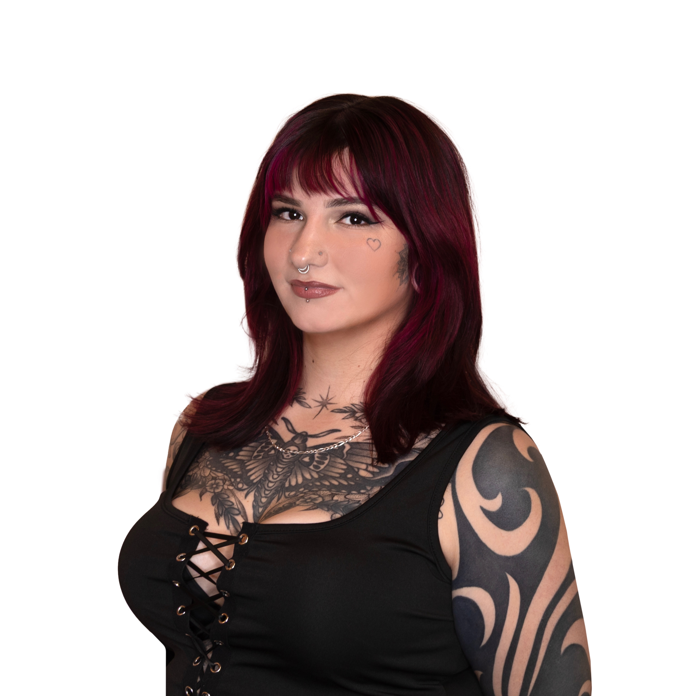 Woman with dark red hair, multiple tattoos on chest and arm, wearing a black lace-up top, and facial piercings.