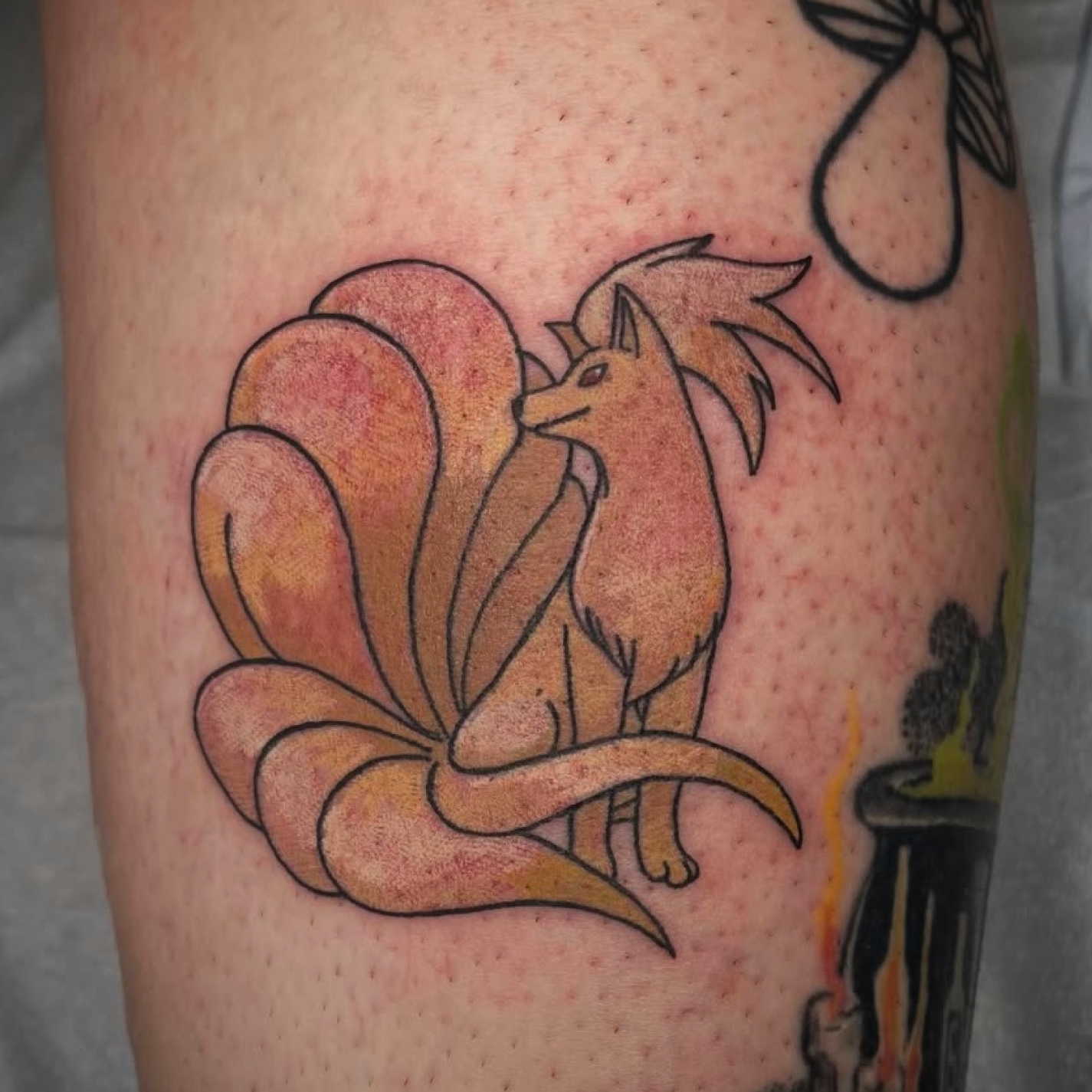 Tattoo of a stylized fox with nine large, curled tails on skin.