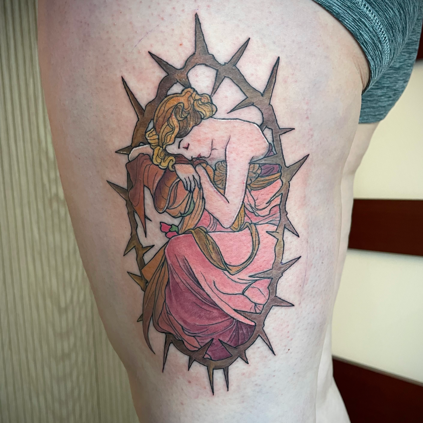 Tattoo of a woman with flowing hair in a pink dress, curled up and surrounded by a frame of sharp thorns.
