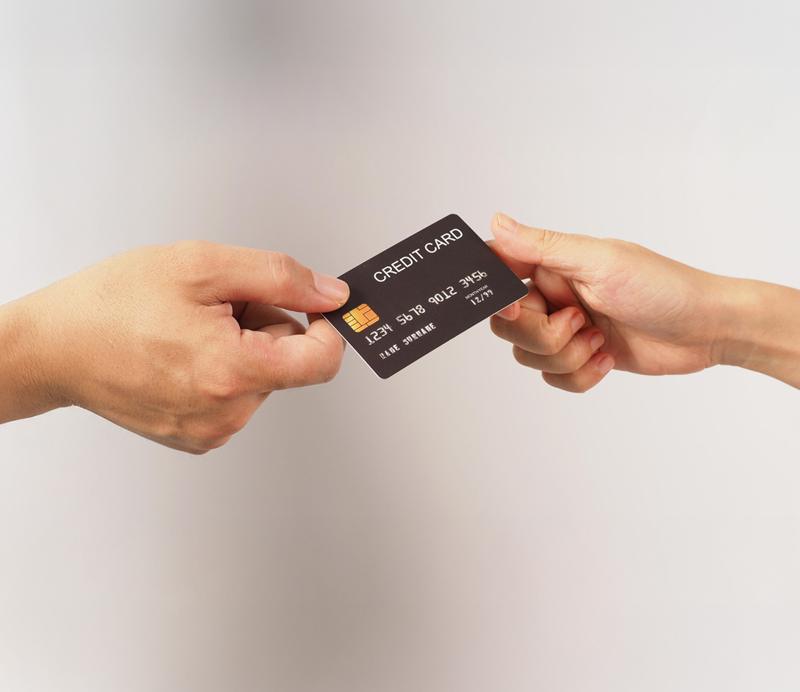 Two hands exchanging a black credit card with chip and embossed numbers.