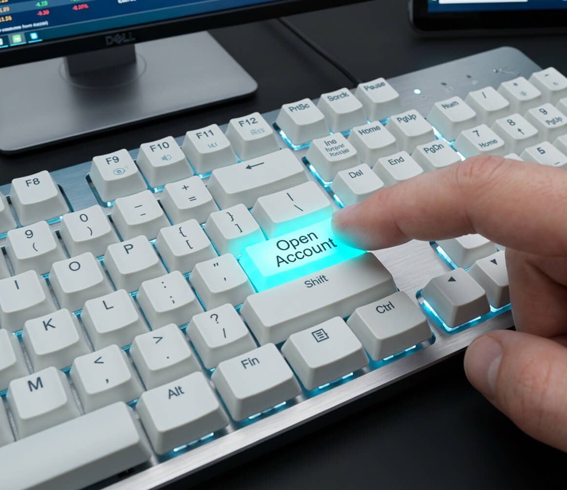 Close-up of a finger pressing a glowing 'Open Account' key on a white computer keyboard with a Dell monitor in the background.