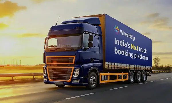 Blue and orange truck driving on a highway at sunset with a banner stating WheelsEye India's No.1 truck booking platform.
