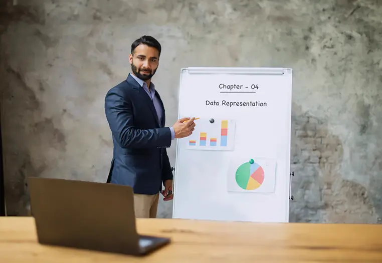 Man in a blazer pointing to a whiteboard with charts and text 'Chapter - 04 Data Representation' during a presentation.