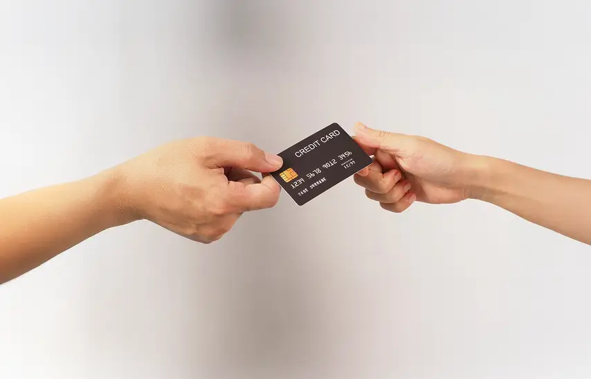 Two hands exchanging a black credit card with chip and embossed numbers.