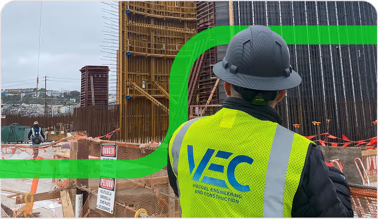 BIM specialist wearing a VEC safety vest and hard hat stands at a jobsite with a large metal framework and wooden forms, looking at the ongoing construction.