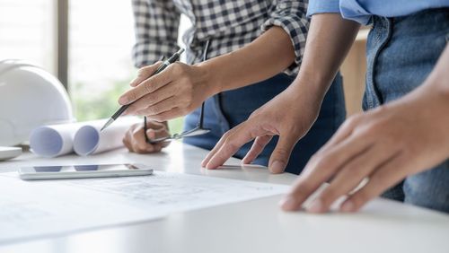 Multiple designers working together on a white desk with architectural drawings.