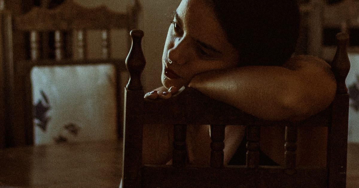 Foto con efecto análgo de una chica pensativa sentada en una silla de madera en la cocina, con la cara apoyada en el respaldo