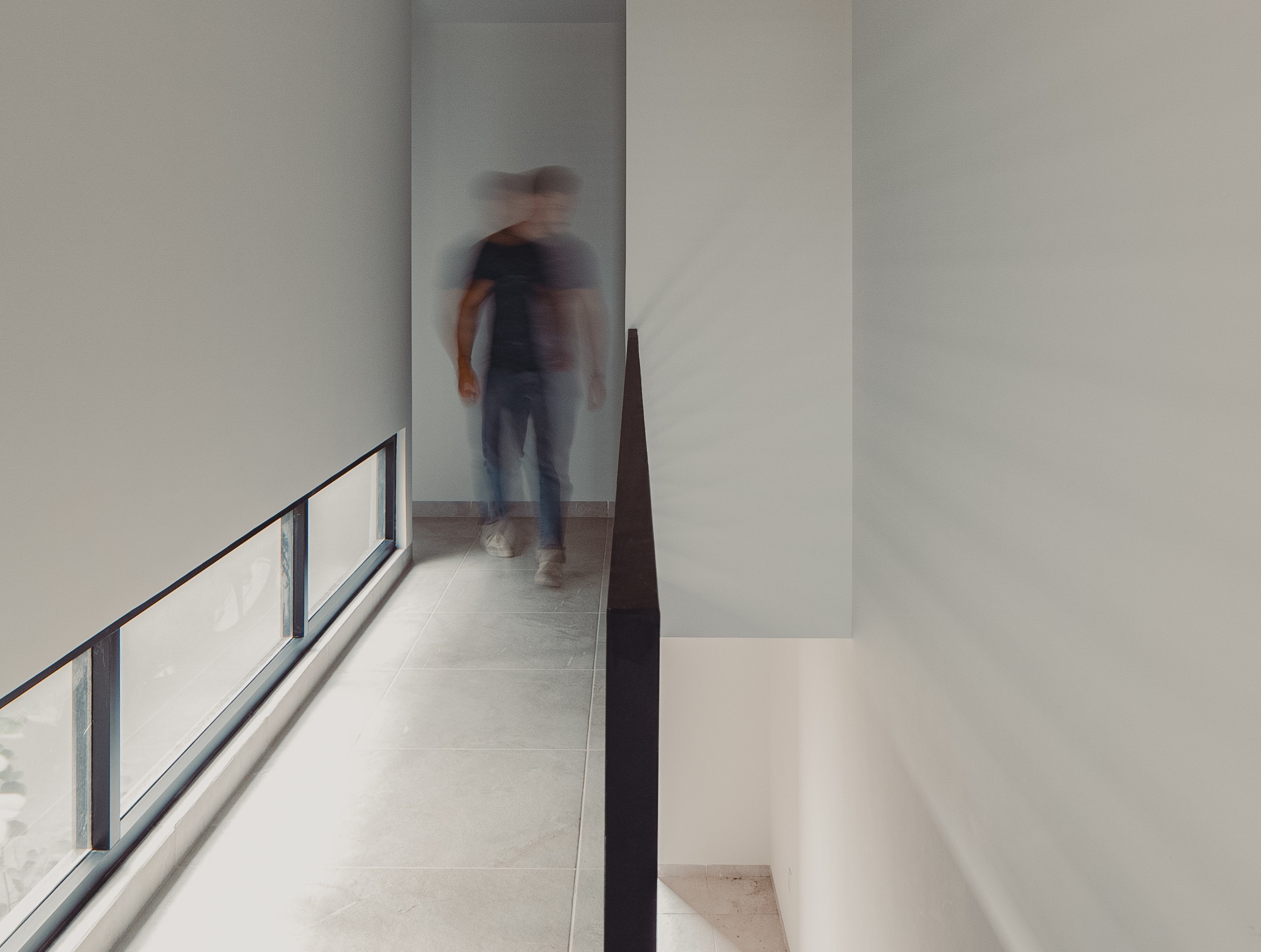 Hombre caminando en un pasillo, casa monocromática y ventanas a nivel de piso barandal negro de herrería simple