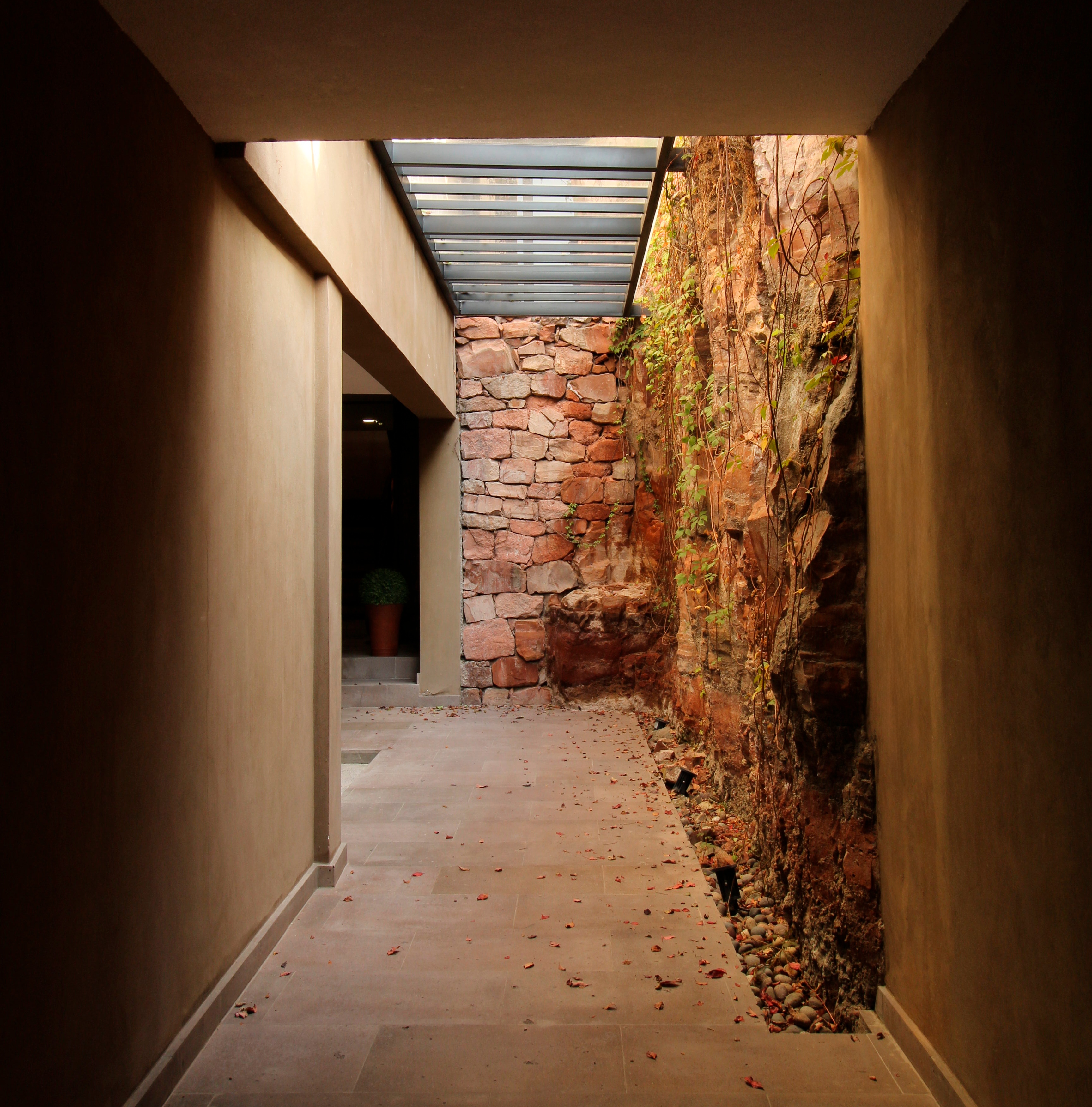 Entrada con lenguaje natural muro de piedra y cantera de fondo tonalidades beige y vegetación que crece del muro