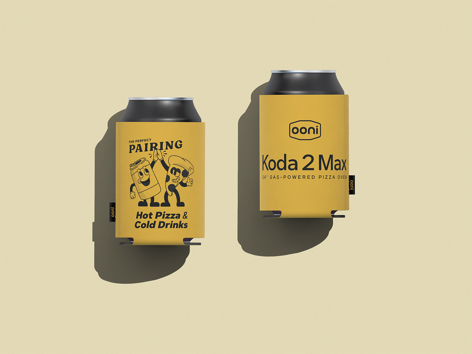Two black cans in yellow sleeves, one with cartoon pizza and drink characters and text 'THE PERFECT PAIRING Hot Pizza & Cold Drinks', the other with 'ooni Koda 2 Max 24" Gas-Powered Pizza Oven'.