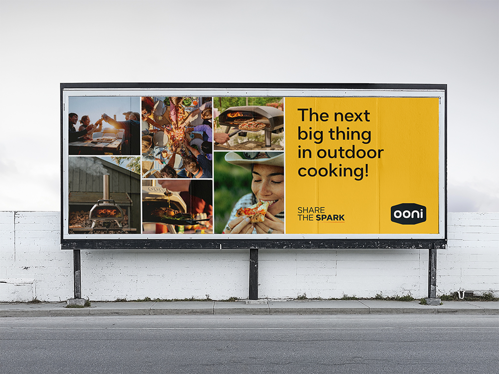 Billboard featuring outdoor cooking scenes with people sharing pizza and a wood-fired oven, with text ‘The next big thing in outdoor cooking! SHARE THE SPARK’ and Ooni logo on a yellow background.