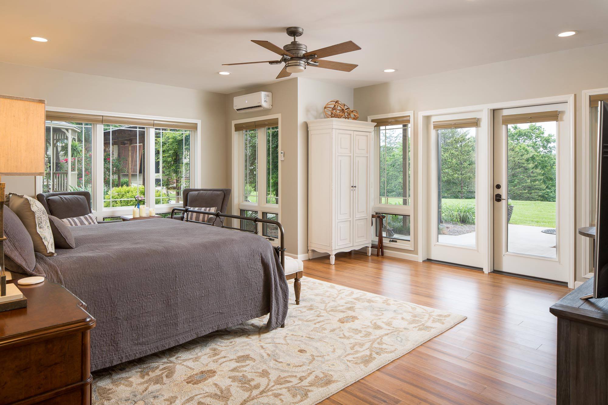 Inside a room at Lucille's Mountain Top Inn & Spa in Sautee Nacoochee, Georgia. The room is veryhomey, with clean lines, lots of tall windows peering out to green foliage, a cozy patterned rug, wood details and a bed covered in a warm-toned gray comforter.