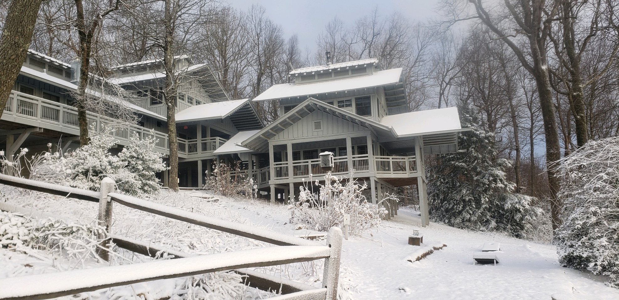A snow-dusted scene of the Hike Inn in Dawsonville, Georgia. There are two building structures next to each other, multiple-storied with windows and patios. Beside and behind the hotel's structure are towering, bare trees.