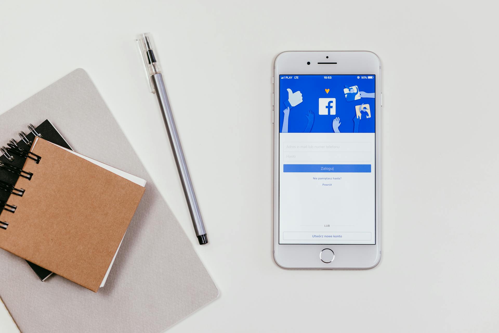 An iPhone opened on the Facebook login page, and notepads and a pen next to it