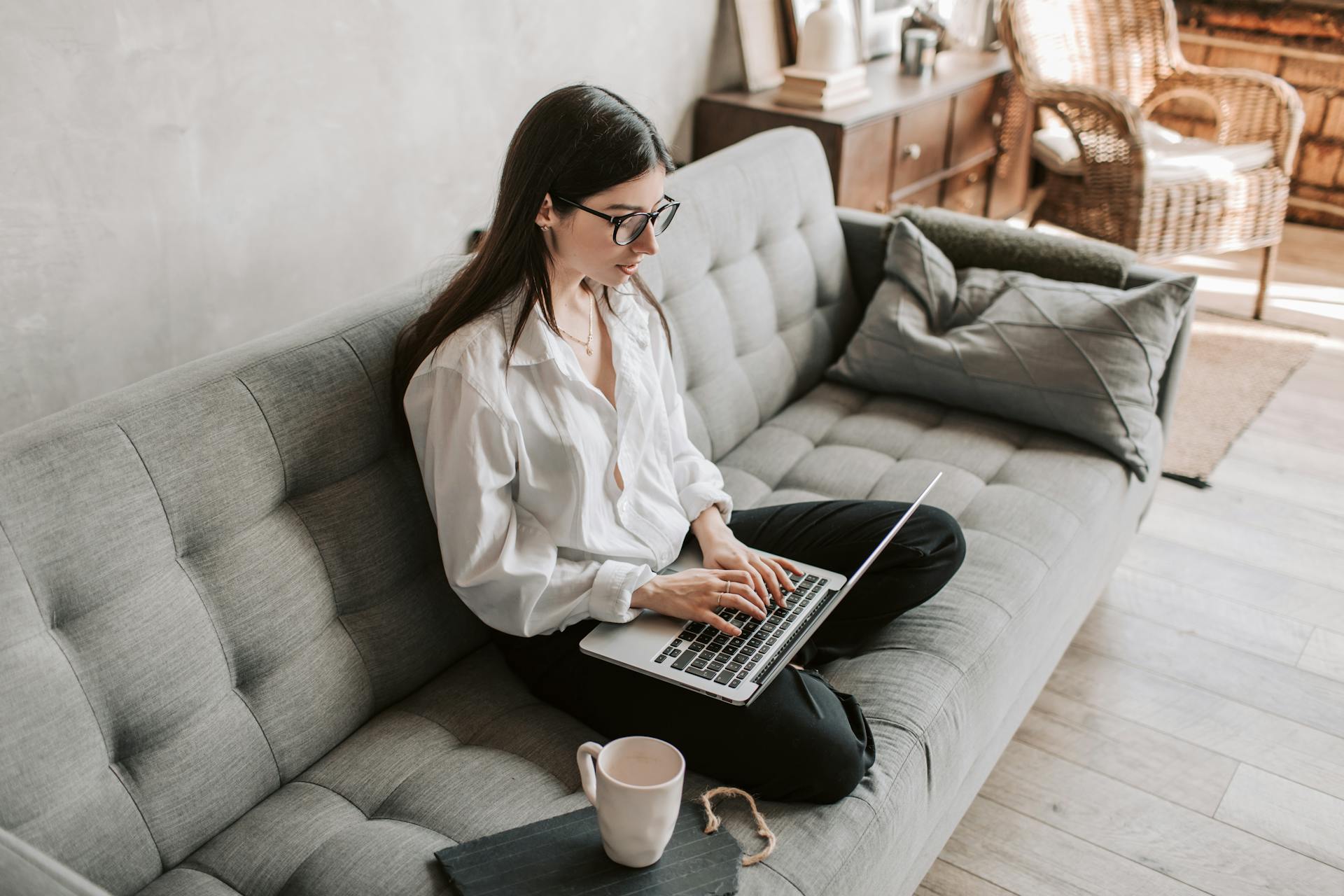A woman sitting on a sofa and typing on a laptop 