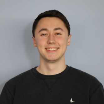 Smiling young man with short dark hair wearing a black sweatshirt against a gray background.