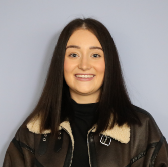 Young woman with straight dark brown hair smiling, wearing a brown jacket with a shearling collar and a black top.
