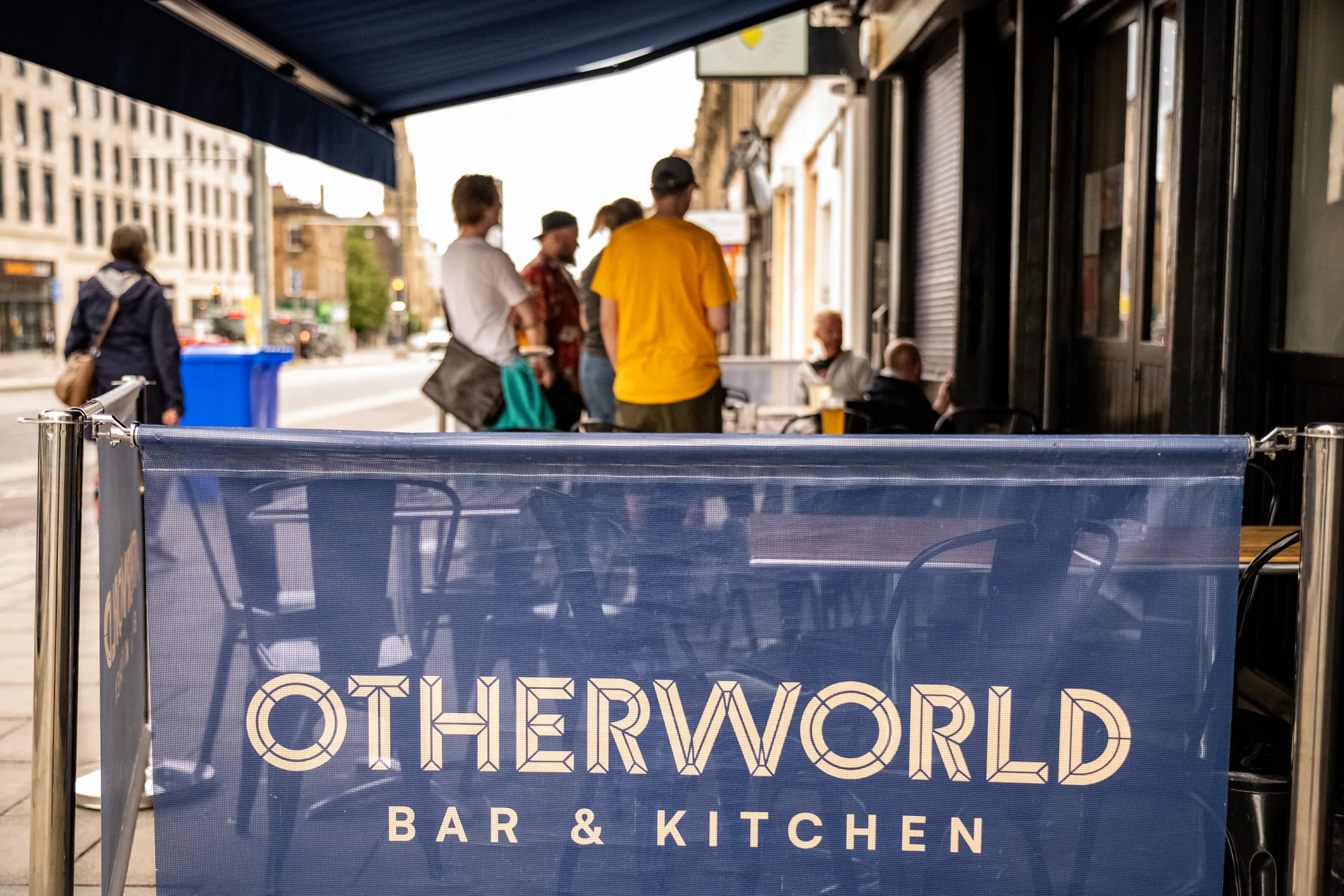People outside Otherworld Bar & Kitchen on Leith Walk, behind the branded terrace screen.