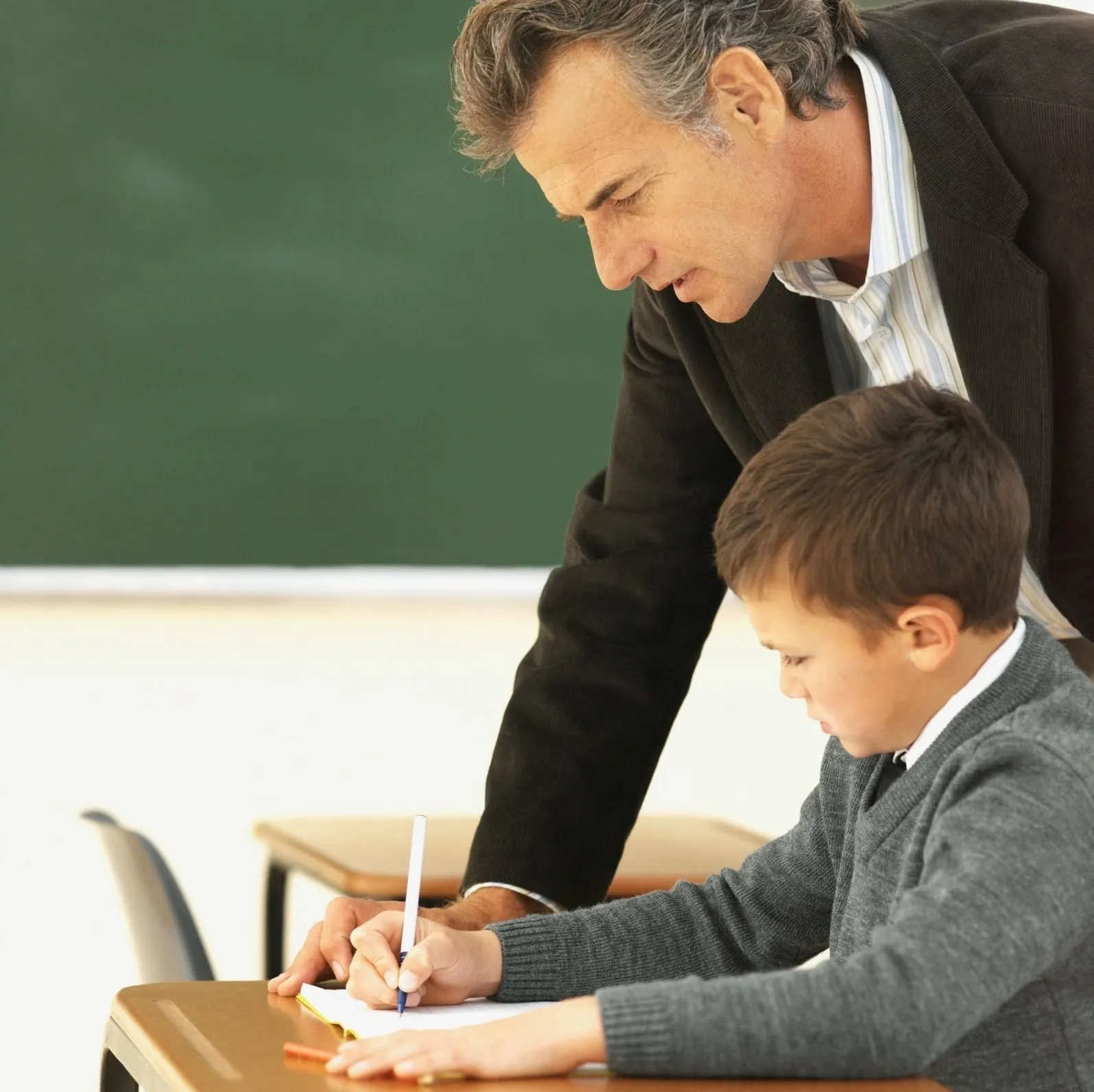 A man teaching a young boy how to write. - New Leaders Images