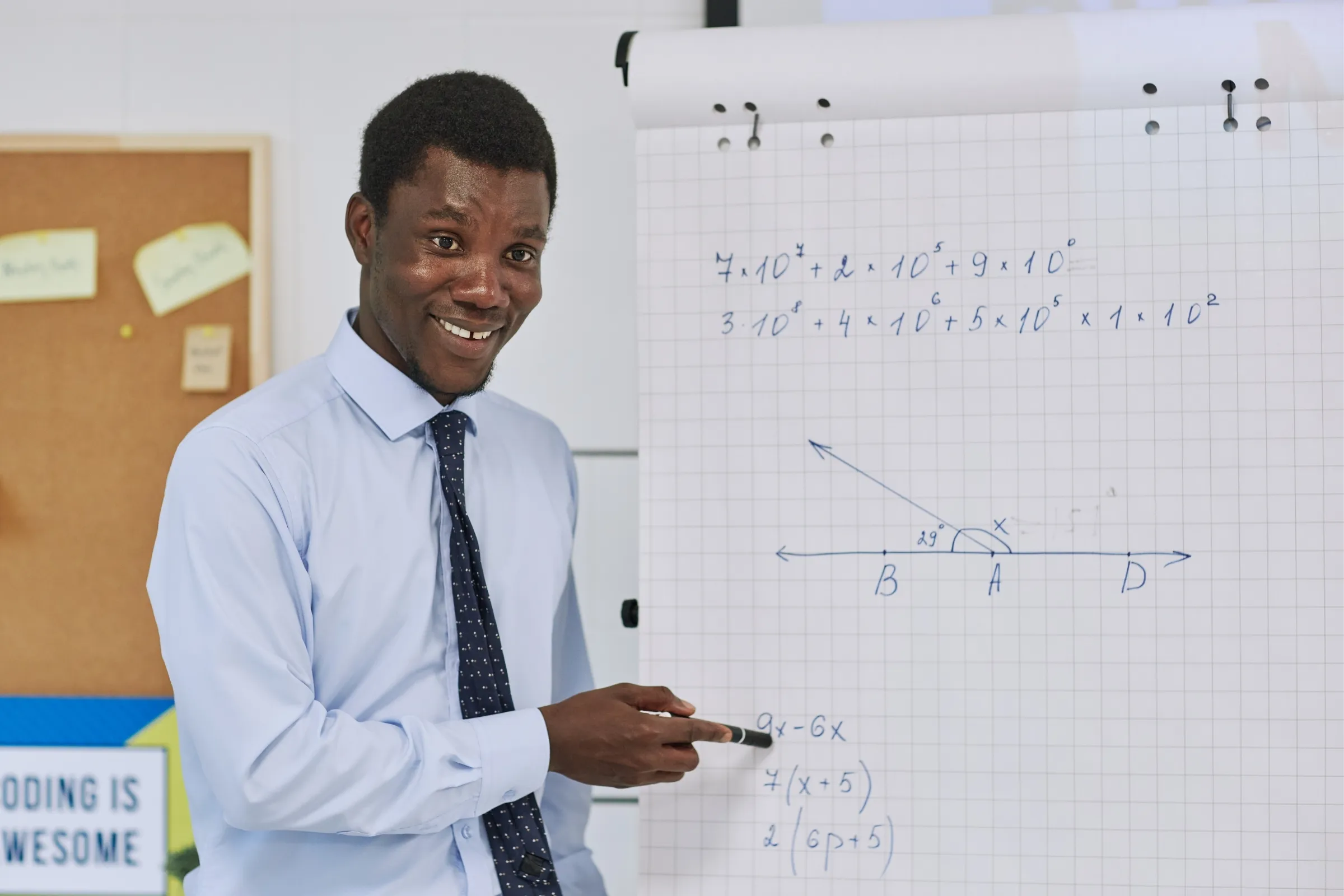 A man wearing a blue shirt and tie pointing at a white board with math problems. - New Leaders Images
