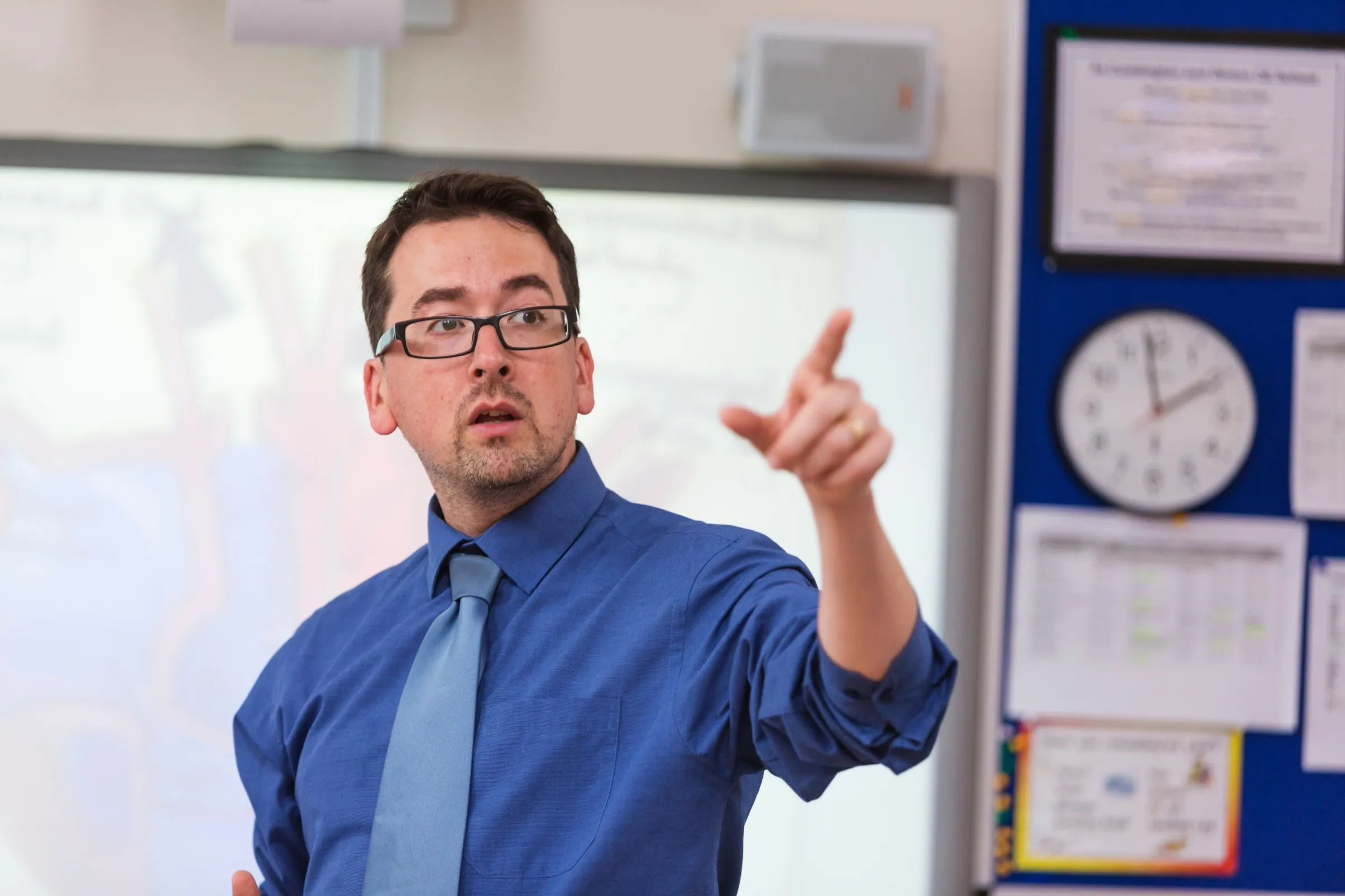 A man in a blue shirt and tie pointing at a white board. - New Leaders Images