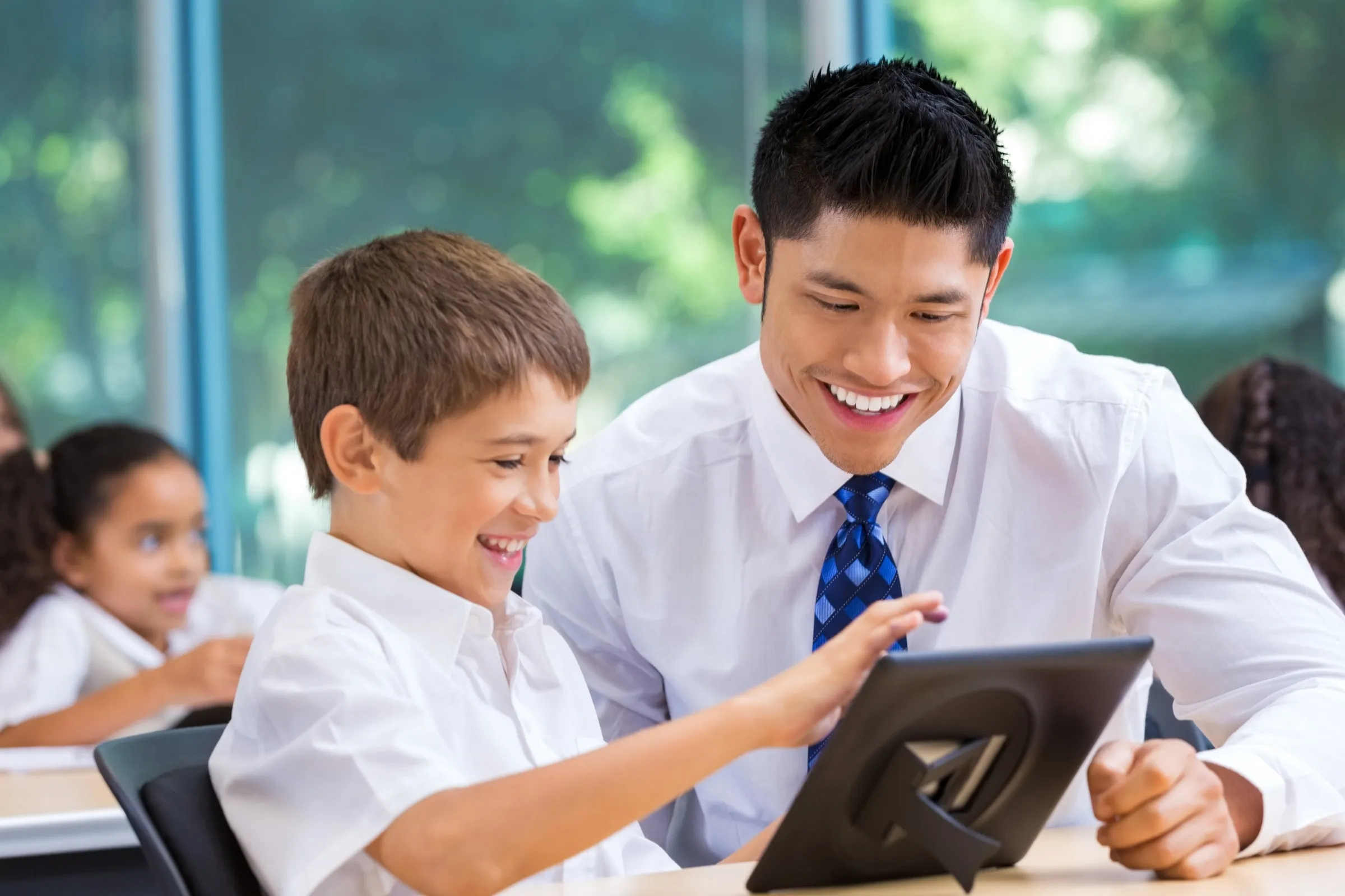 A man and a boy are smiling and looking at a tablet computer. - New Leaders Images