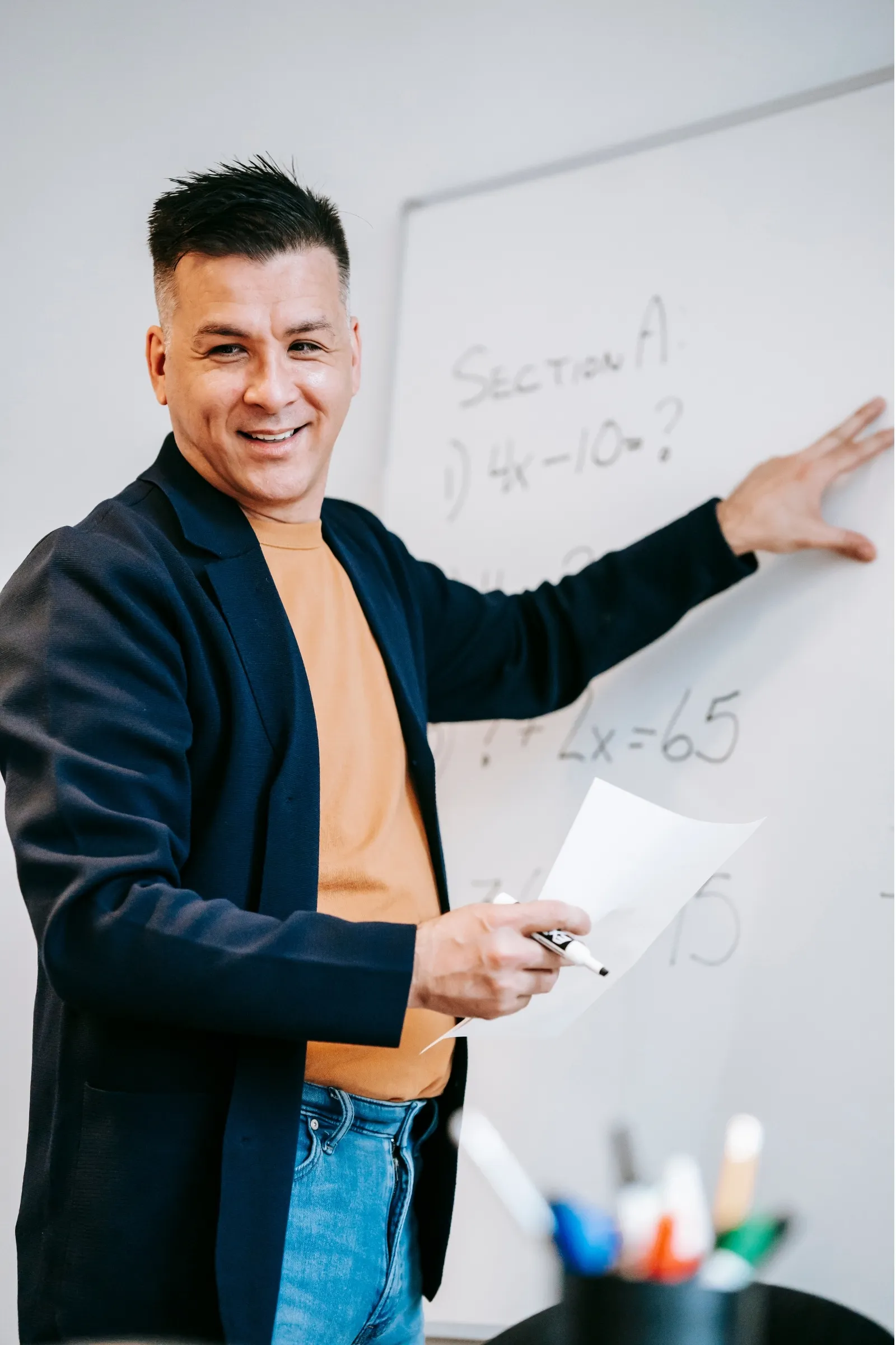 A man in a blue jacket and orange shirt writing on a whiteboard. - New Leaders Images