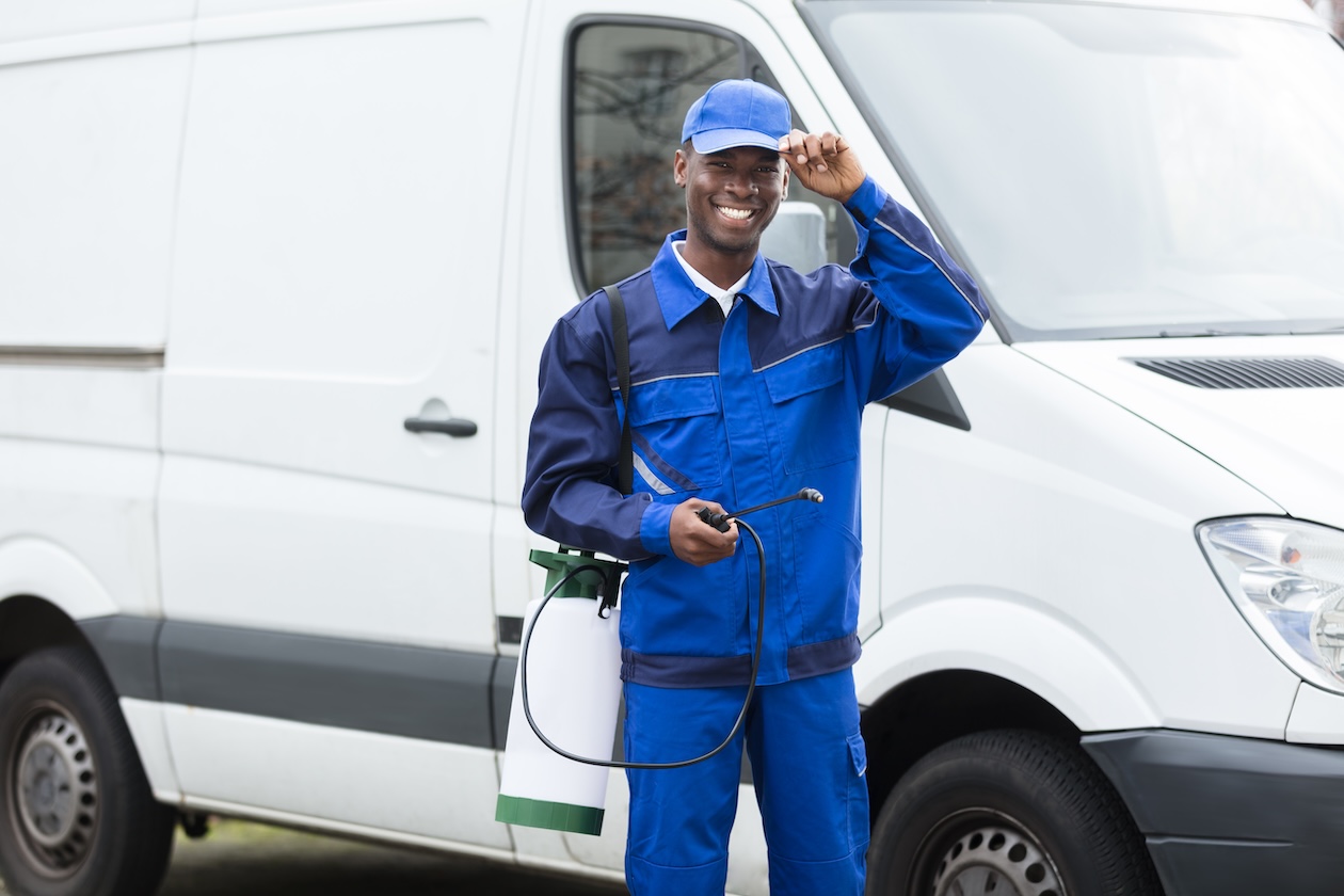 Young smiling pest control technician holding a pesticide sprayer.