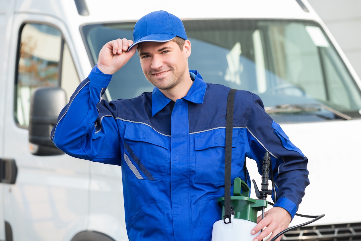 Confident pest control worker wearing a cap standing in front of a service truck, representing professionalism and reliability in field service