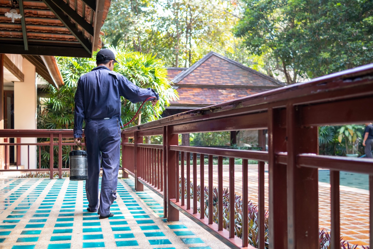 Pest control worker spraying exterior insect treatment around a customer’s home while inspecting for termite activity and documenting preventative pest control service.