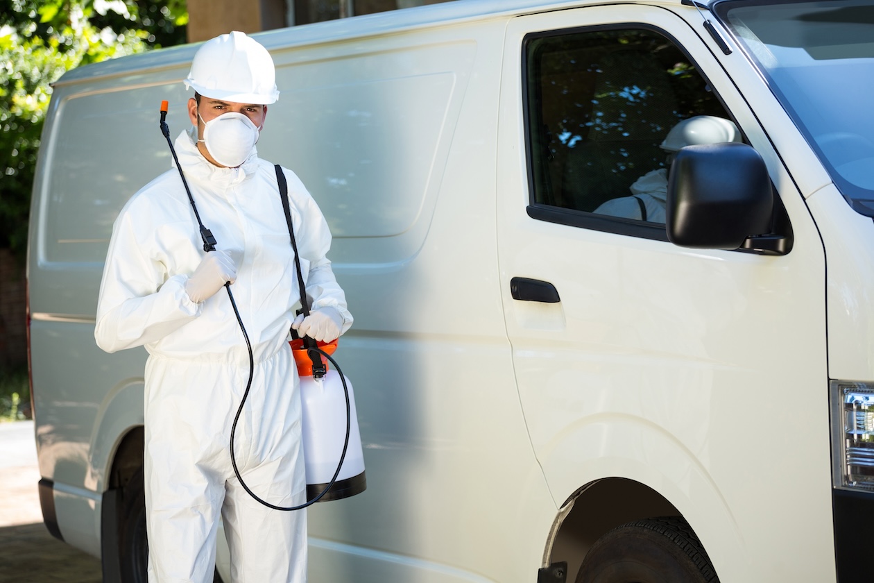 Portrait of a pest control technician standing beside a company service van while preparing for residential pest treatment services.