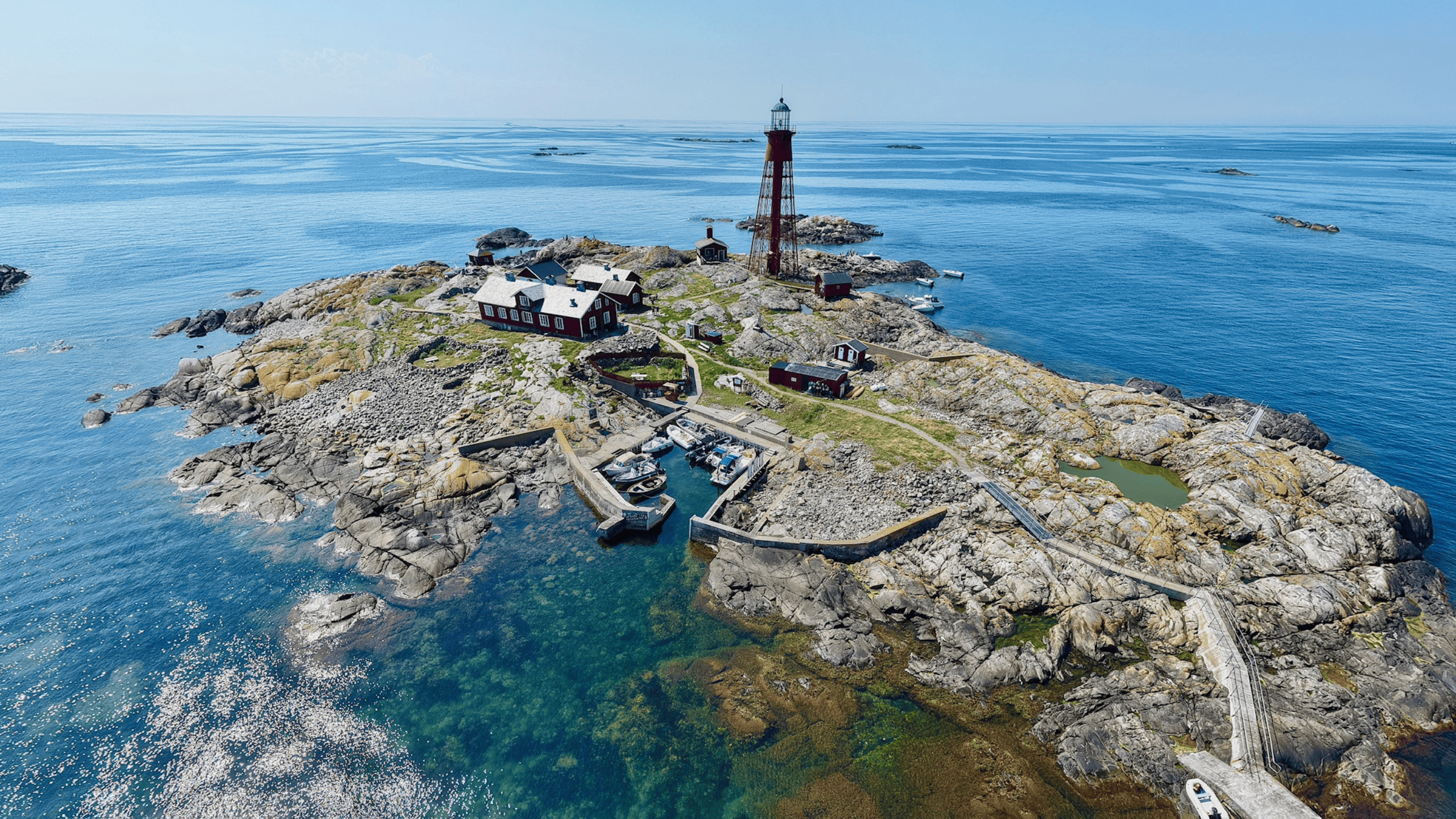 aerial view of an island in the sea with a red lighthouse, red houses, and small boats in the harbor