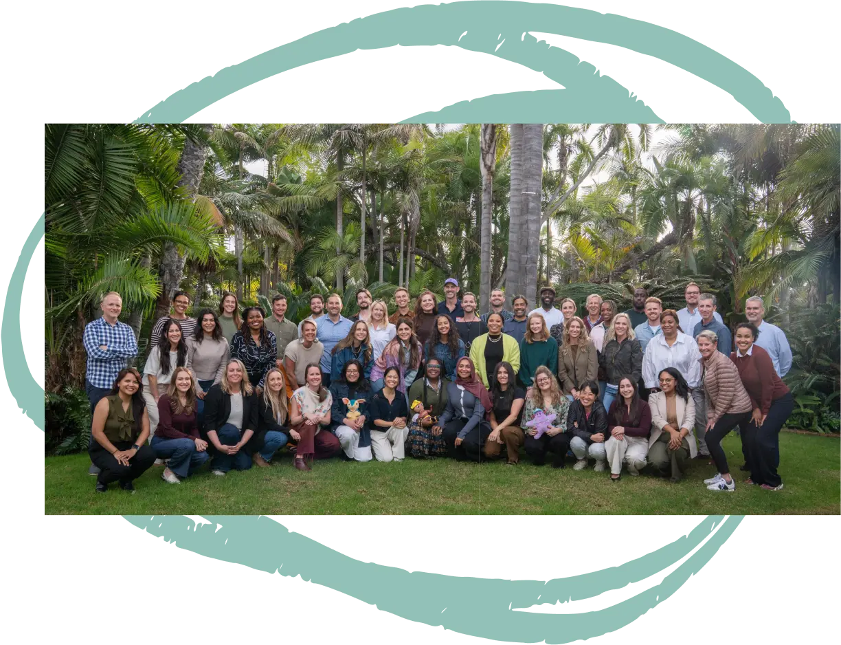 Group photo of around 50 diverse adults posing outdoors on grass with tropical trees in the background.