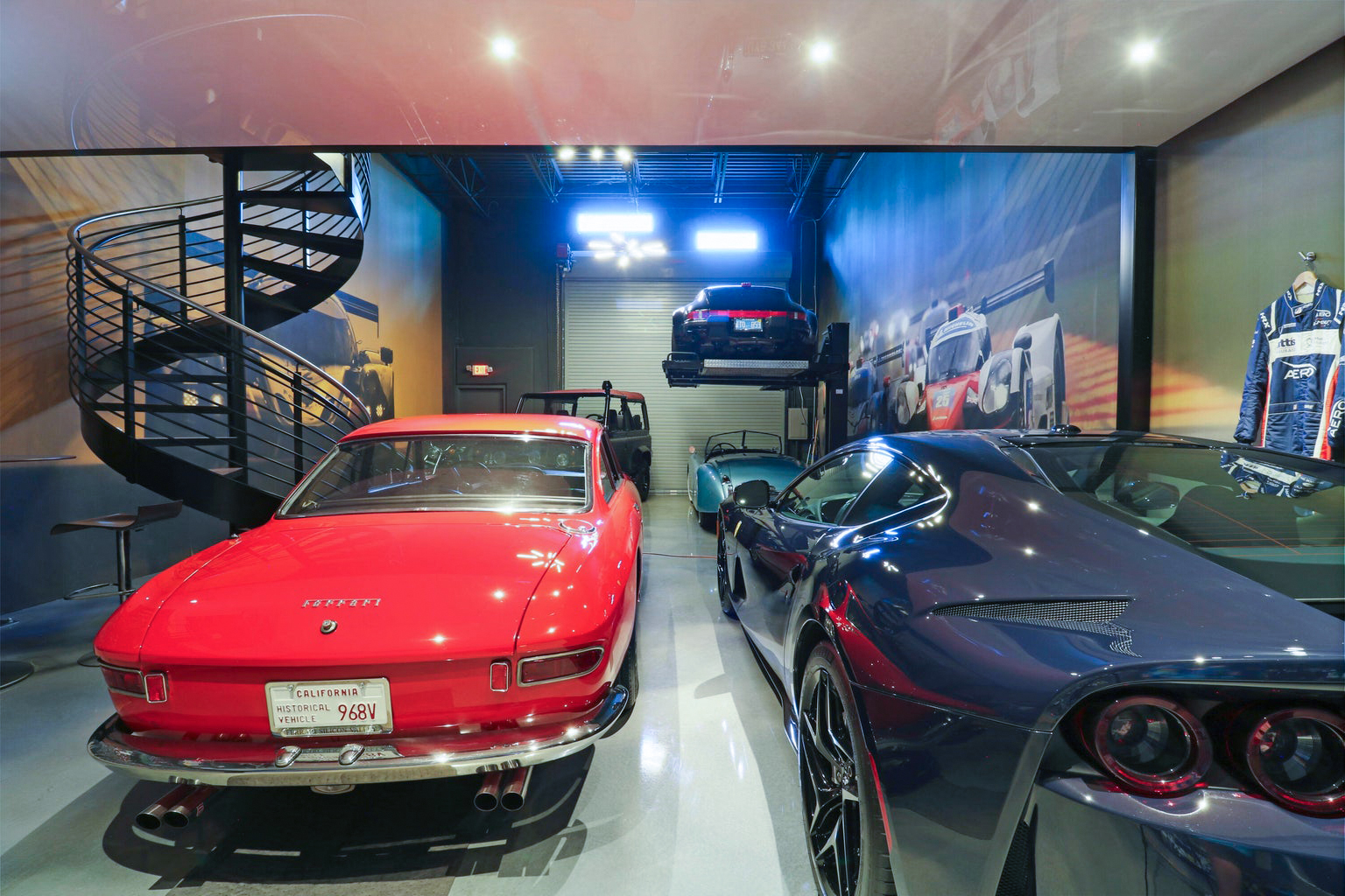 Interior of a modern garage featuring a red classic Ferrari, a dark luxury sports car, a black SUV, a light blue vintage convertible, and a black car on a hydraulic lift under bright ceiling lights.